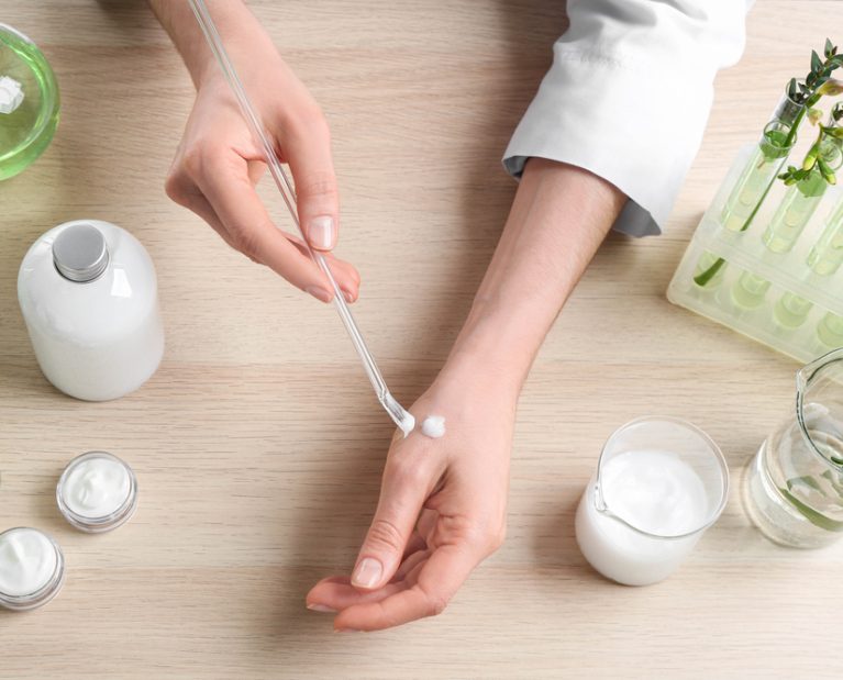 Woman applying natural cream onto hand in cosmetic laboratory, above view